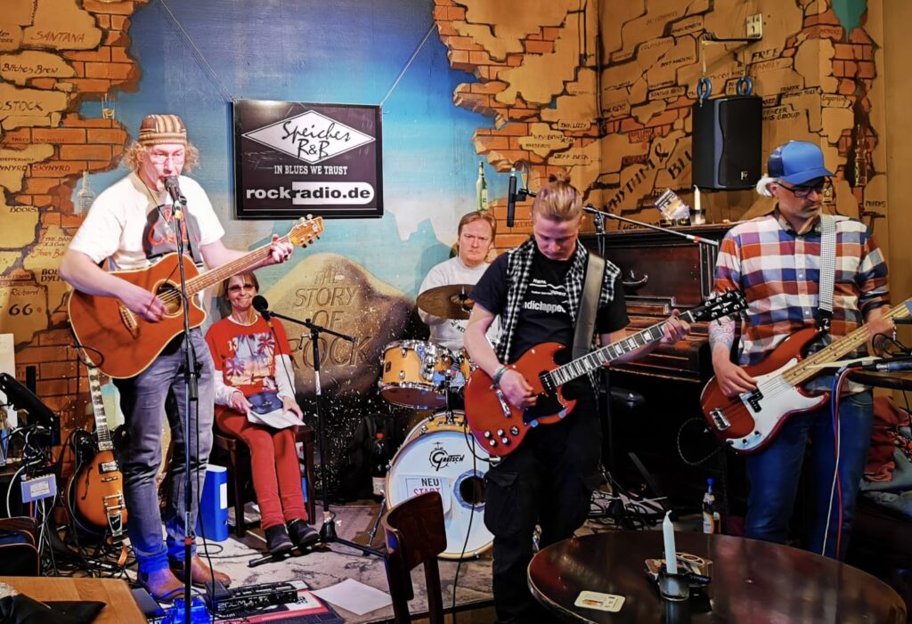 5 Mitglieder der Band live auf der Bühne in einer Kneipe.