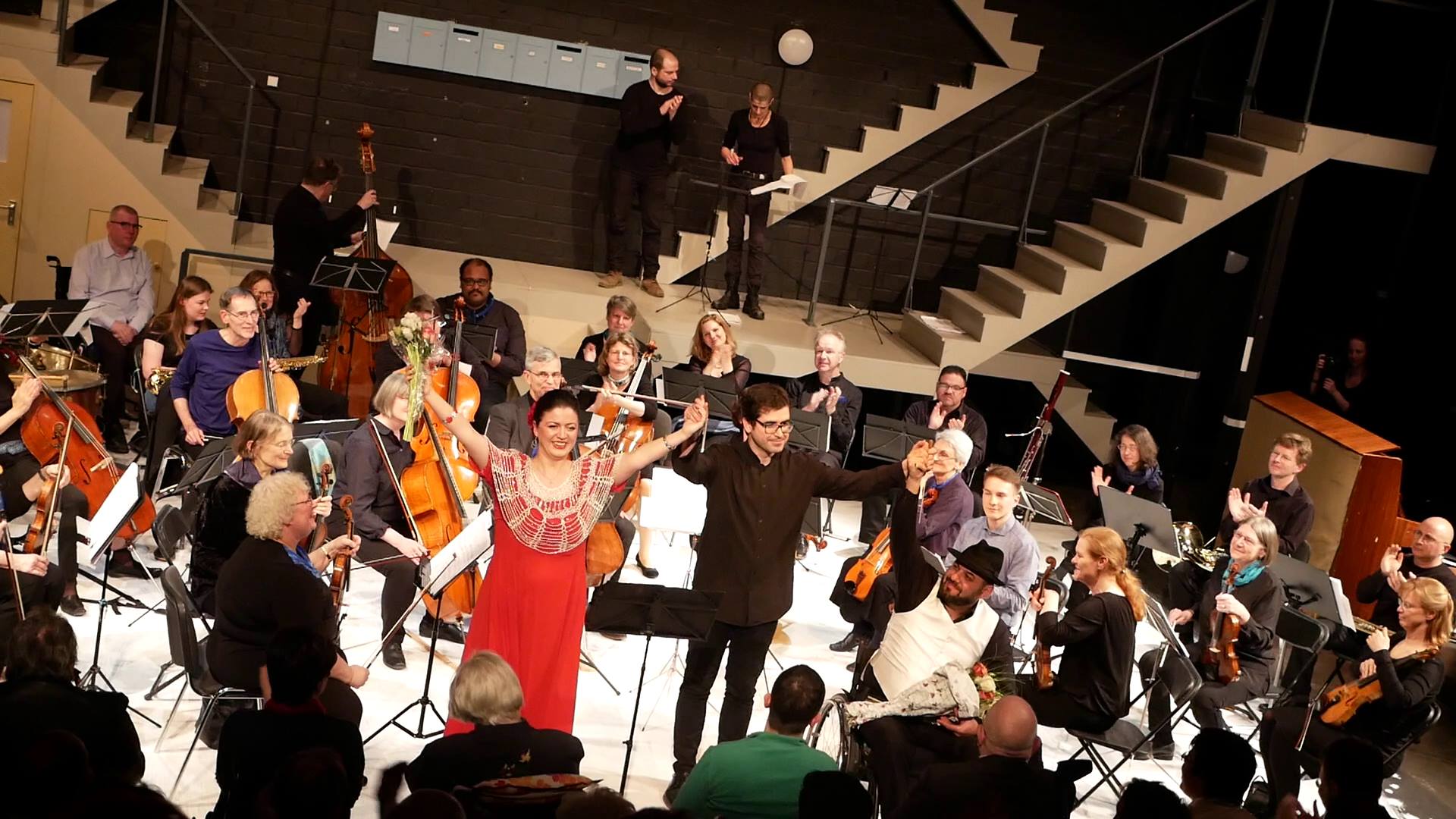 Das Foto zeigt das Utopia Orchester beim Schlussapplaus nach dem Konzert am 30.4.2019 im Berliner GRIPS Theater. Vor dem Orchester sieht man den Dirigenten Mariano Domingo mit zwei tollen Gesangs-SolistInnen: Kristina Gordadze und Artak Kirakosyan.