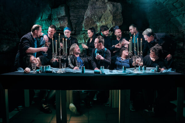 Gruppenfoto der Band Chickpeas in einem gewölbten Felsenkeller, inszeniert im Stil von Da Vincis „Das Letzte Abendmahl“ an einer mit Kerzenleuchtern und Dosen gedeckten Tafel.