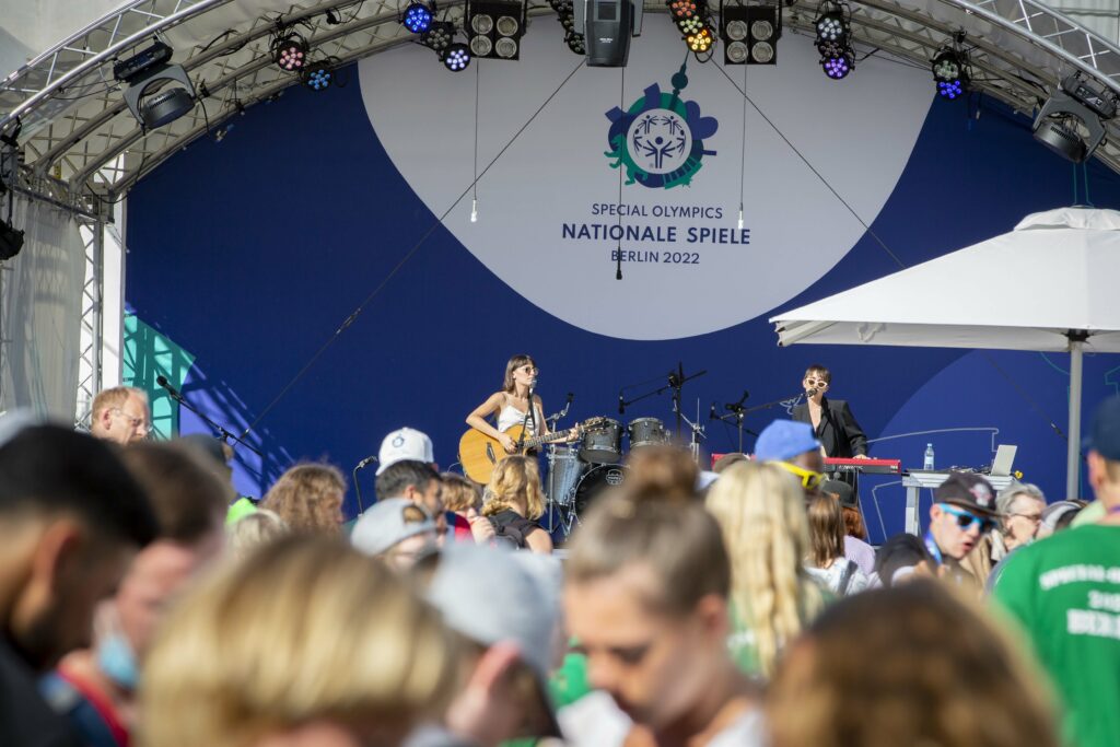 Zwei Musikerinnen auf einer Freilichtbühne, im Hintergrund Special Olympics Schriftzug, vor der Bühne Publikum
