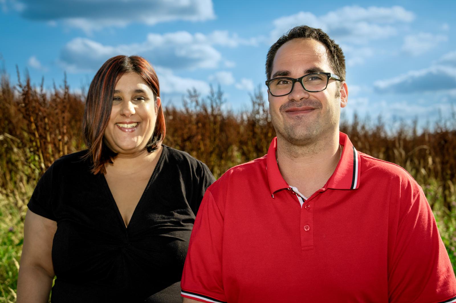 Ein buntes Profilfoto von Alina und Tim. Sie gucken freundlich in die Kamera. Im Hintergund ein Feld und blauer Himmel.