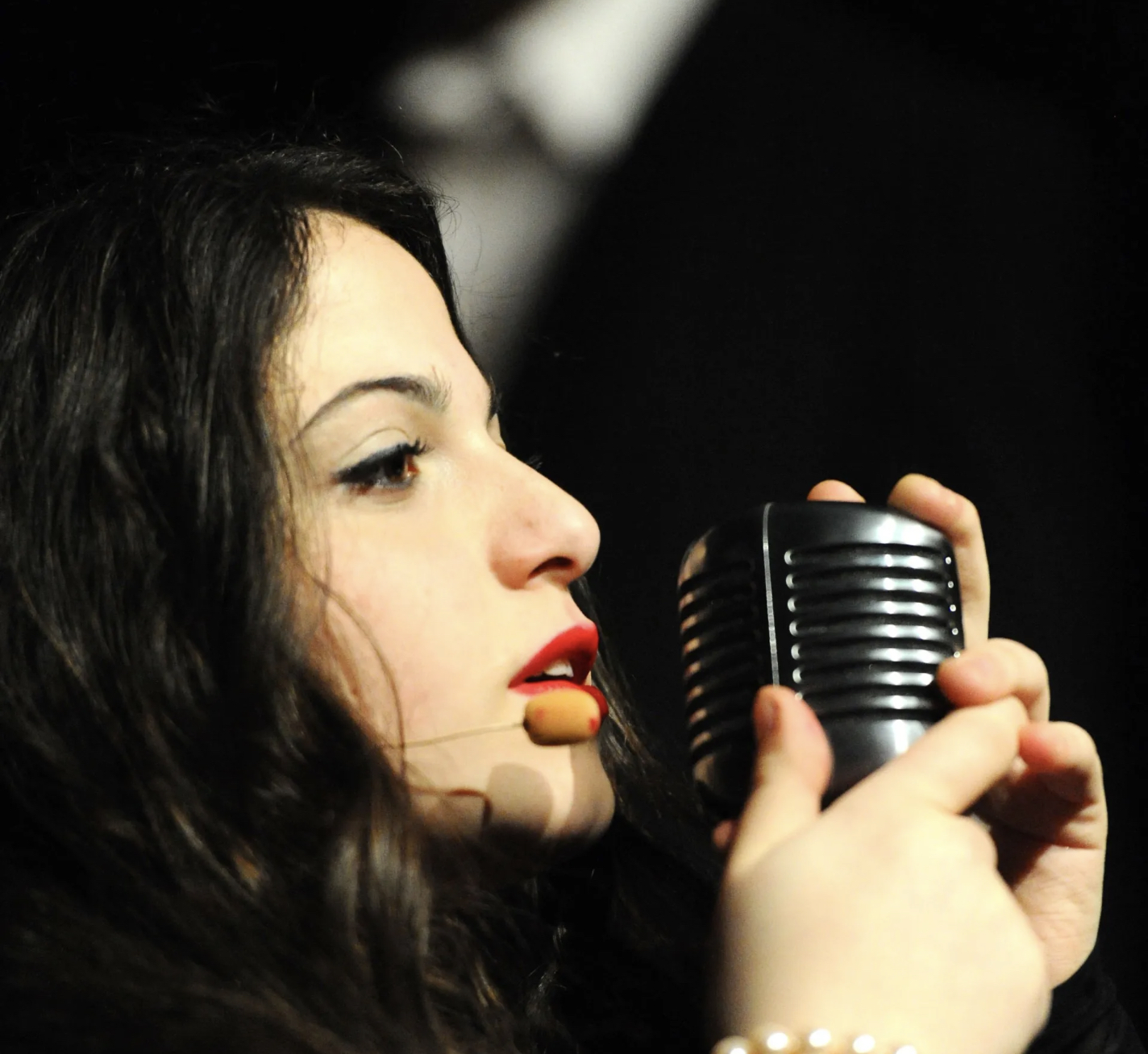 Foto einer Sängerin die in ein Mikrofon singt, dass sie mit beiden Händen umfasst.