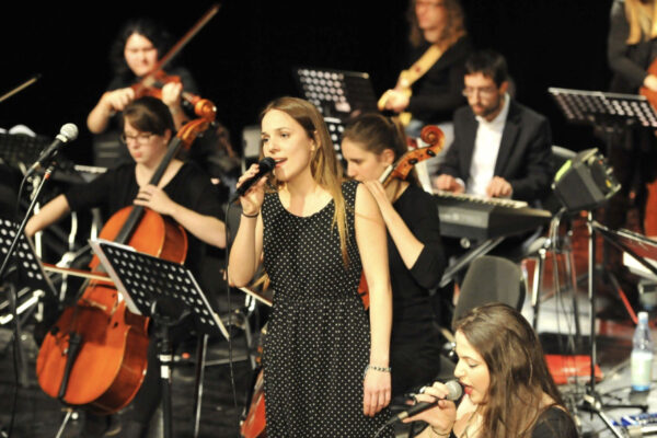 Foto von einem Orchester mit Sängerin live auf der Bühne.