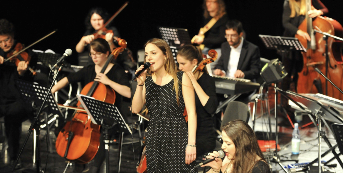 Foto von einem Orchester mit Sängerin live auf der Bühne.