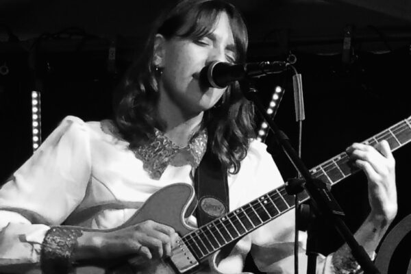 schwarz weiß Foto von Vera singend und Gitarre spielend live auf der Bühne.