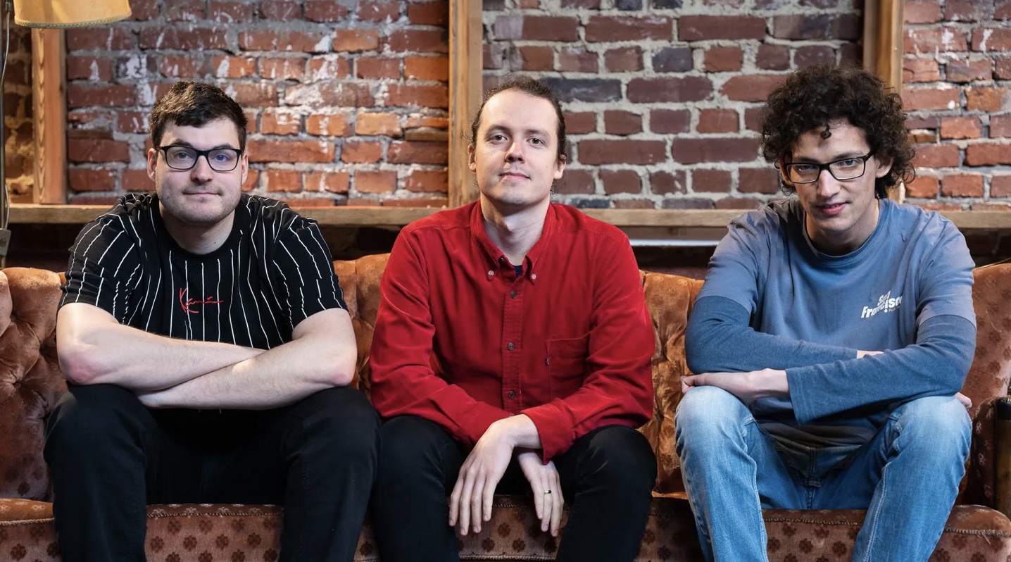 drei Männer sitzen auf einem Sofa und gucken in die Kamera - frontal fotografiert
