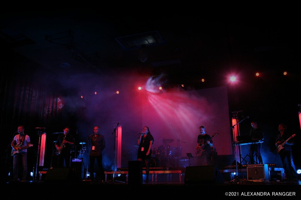 Foto von Band mit acht Mitgliedern live auftretend auf professionell ausgeleuchteter Innenbühne