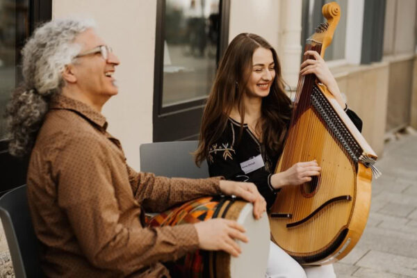 Foto von einem Mann und einer Frau, gut gelaunt auf Saiteninstrumenten spielend