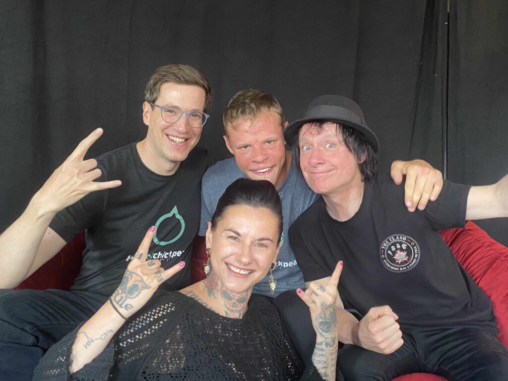 Buntes Foto von vier Menschen: zwei Mitgliedern der Band The Cool Chickpeas zusammenClaudia Lippmann vom Rundfunk-Tanzorchester Ehrenfeld und Vom Ritchie von den Toten Hosen. Alle gucken lächelnd in die Kamera.
