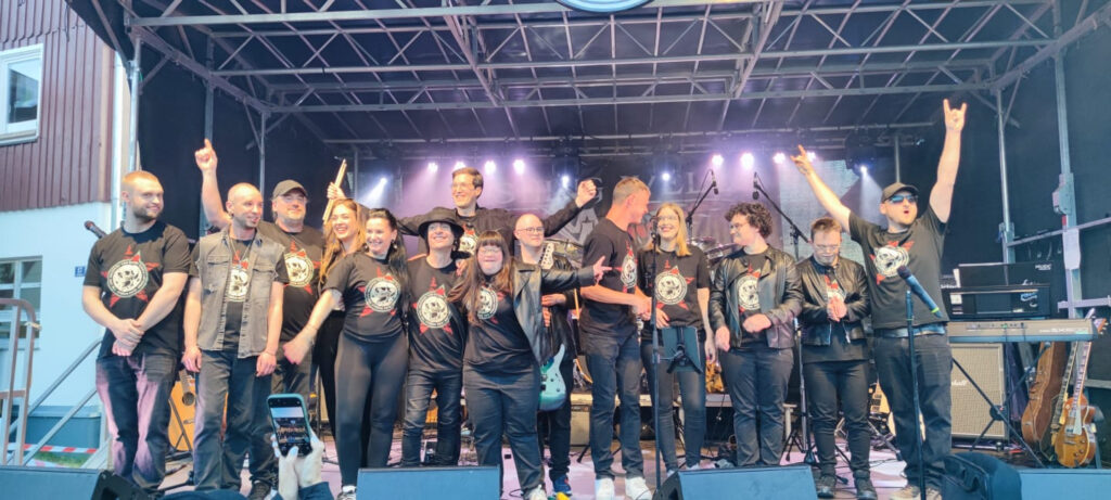 Buntes Foto von der Band The Cool Chickpeas zusammen mit Claudia Lippmann vom Rundfunk-Tanzorchester Ehrenfeld und Vom Ritchie von den Toten Hosen. Alle stehen zum Verbeugen gemeinsam auf einer Außenbühne. Von vorne fotografiert.