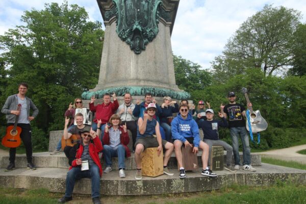 Auf dem Bild ist die Band Mix Music zu sehen. Es sind 15 Menschen mit ihren Instrumenten. Sie haben Gitarren, Trommeln und ein Akkordeon in der Hand.