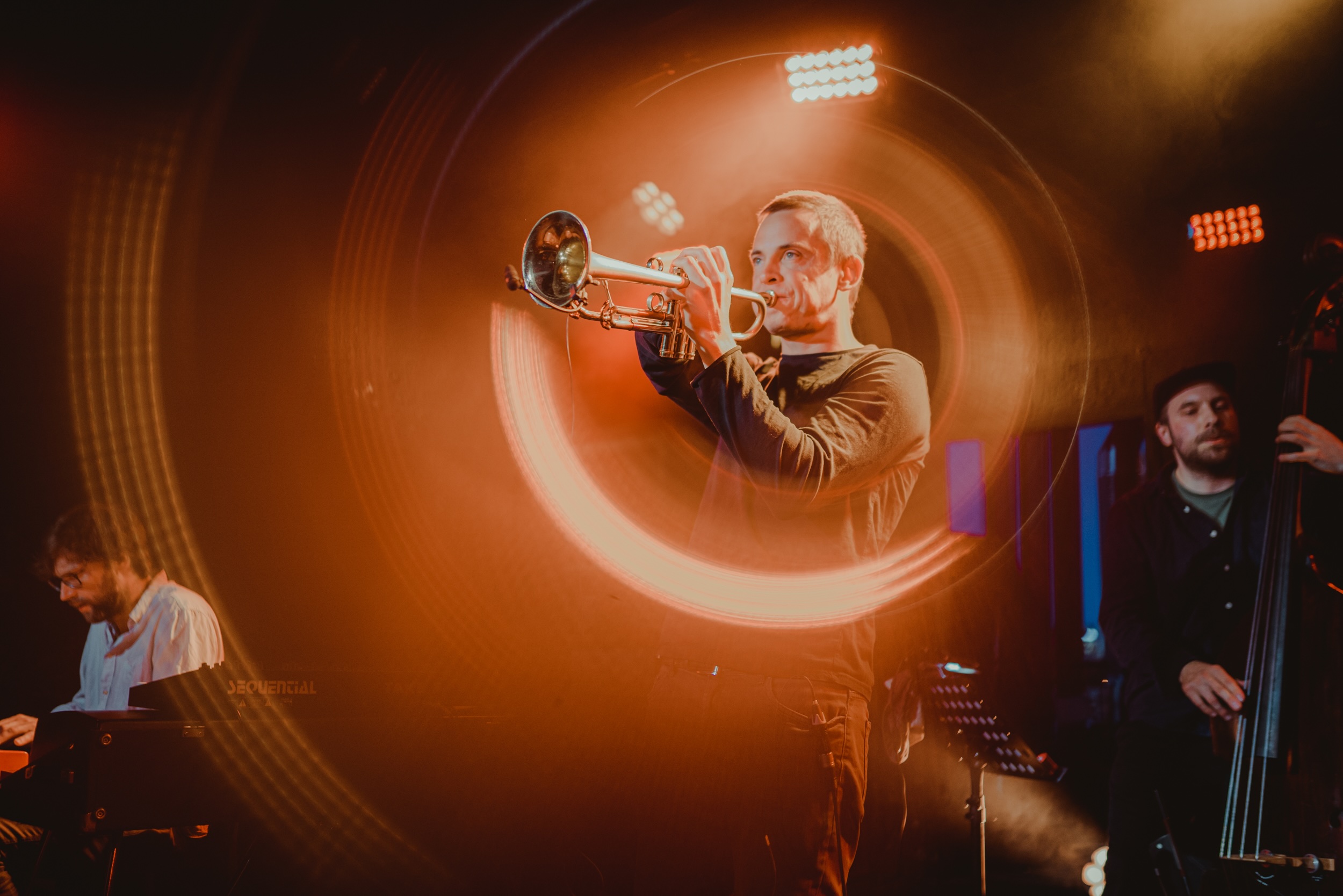 Foto von Barabas Lörinc live auf der Bühne. Er spielt Trompete. Durch einen Foto Effekt zieht die Trompete einen Lichtkreis um seinen Kopf und Oberkörper.