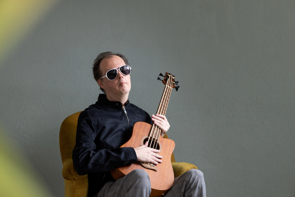Buntfoto von einem sitzenden Gitarristen mit Sonnenbrille.