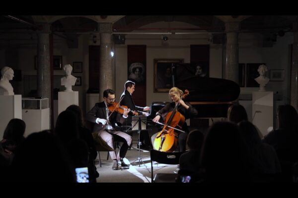 Buntfoto mit drei schick gekleideten Musikern, mit Piano Cello und Violine