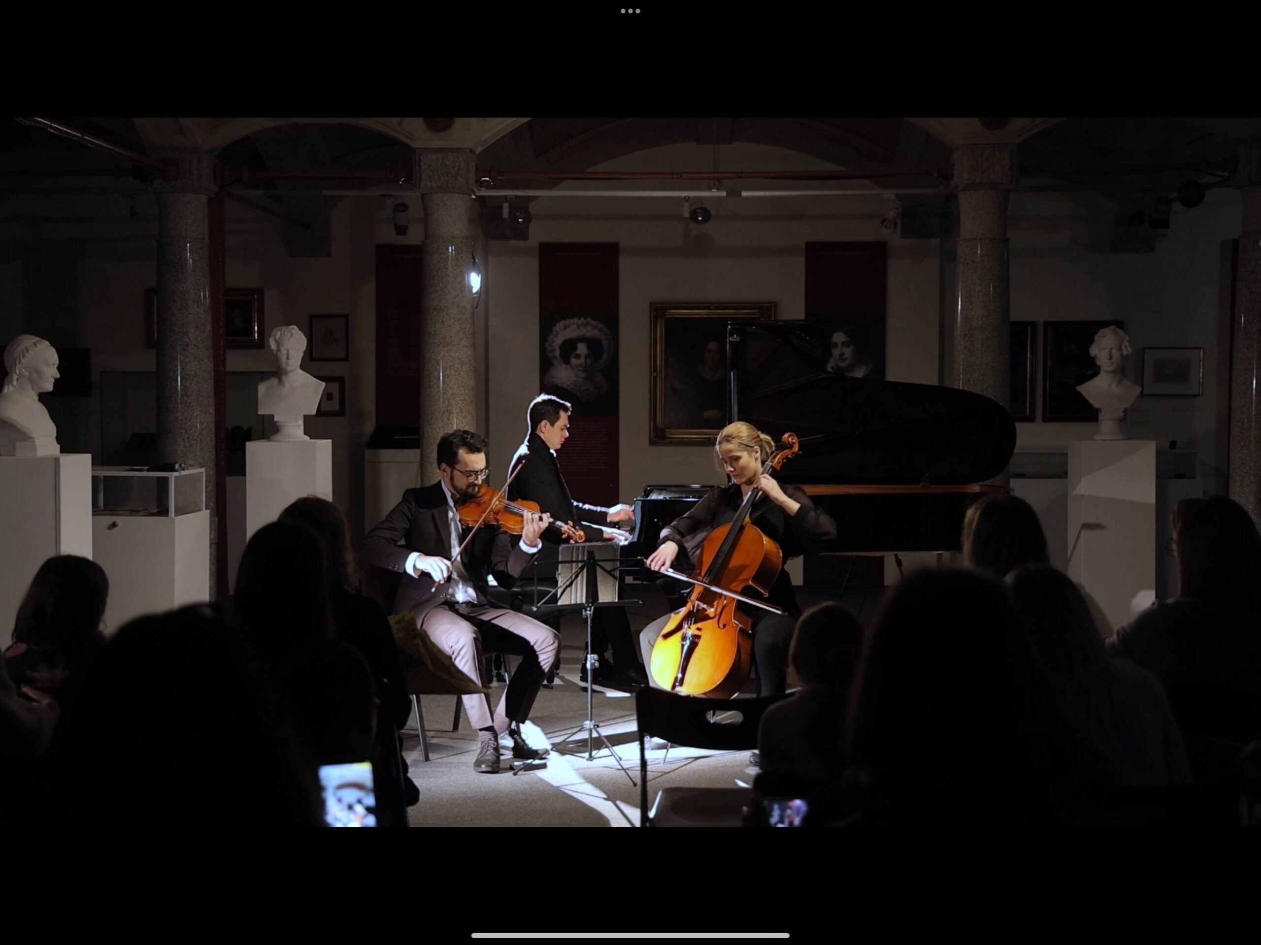 Buntfoto mit drei schick gekleideten Musikern, mit Piano Cello und Violine