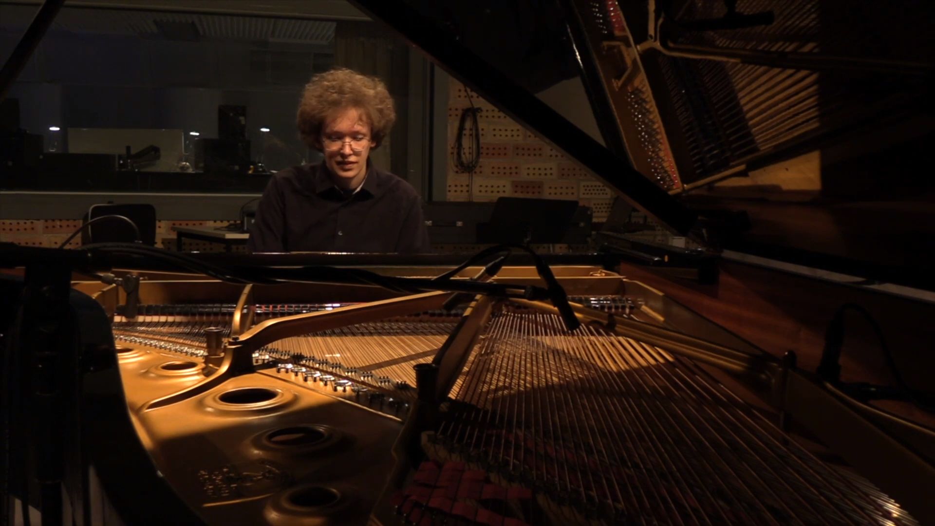 Buntfoto von einem jungen Mann an einem Flügel, durch den aufgeklappten Deckel des Flügels hindurch fotografiert.